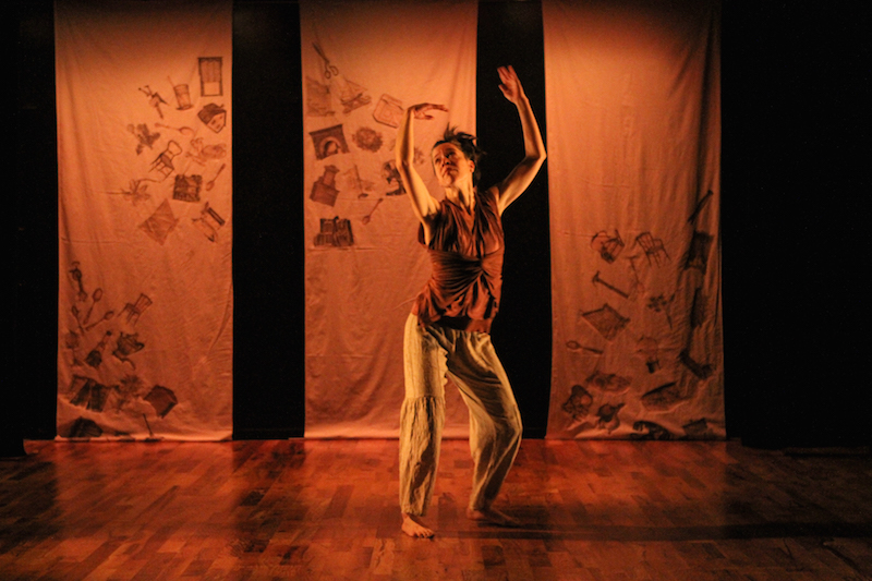 Donna Costello bats her arms above her head in front of the canvas triptych